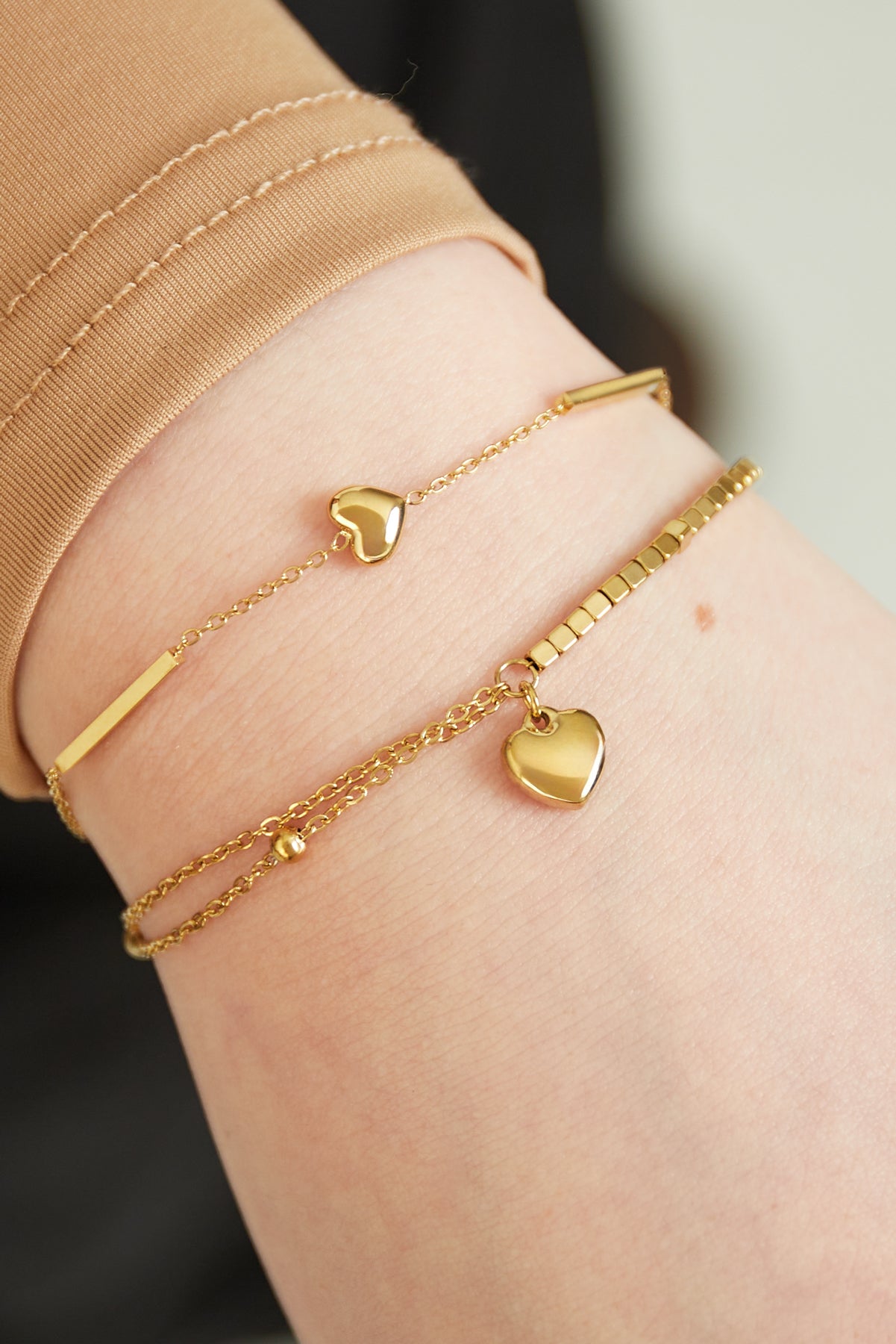 Close-up of woman's wrist wearing stacked bracelets including a gold heart charm bracelet and a beaded one