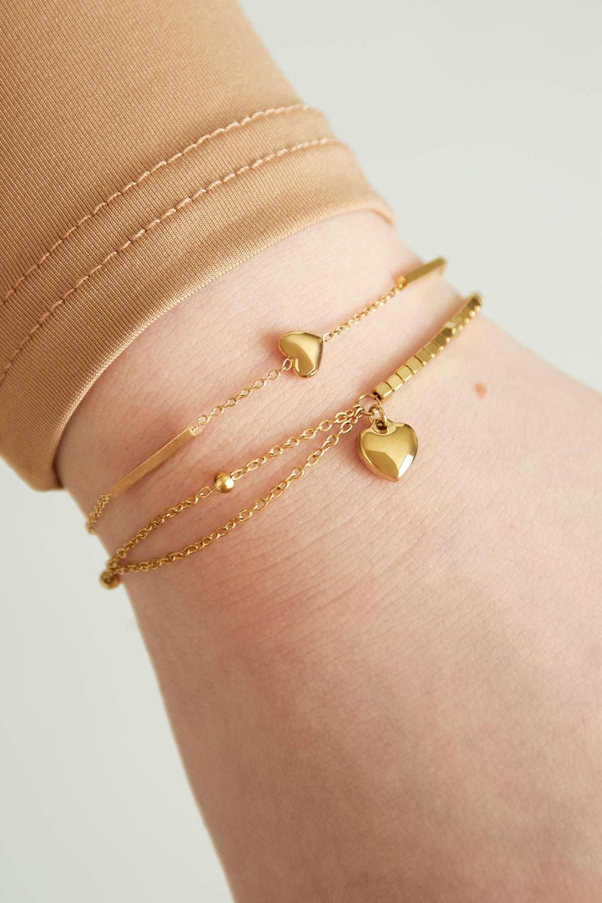 Close-up of gold heart charm bracelet layered with another delicate gold bracelet on wrist