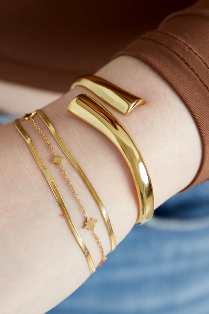 Close-up of layered gold bracelet featuring star charms worn alongside another thick gold cuff bracelet on wrist