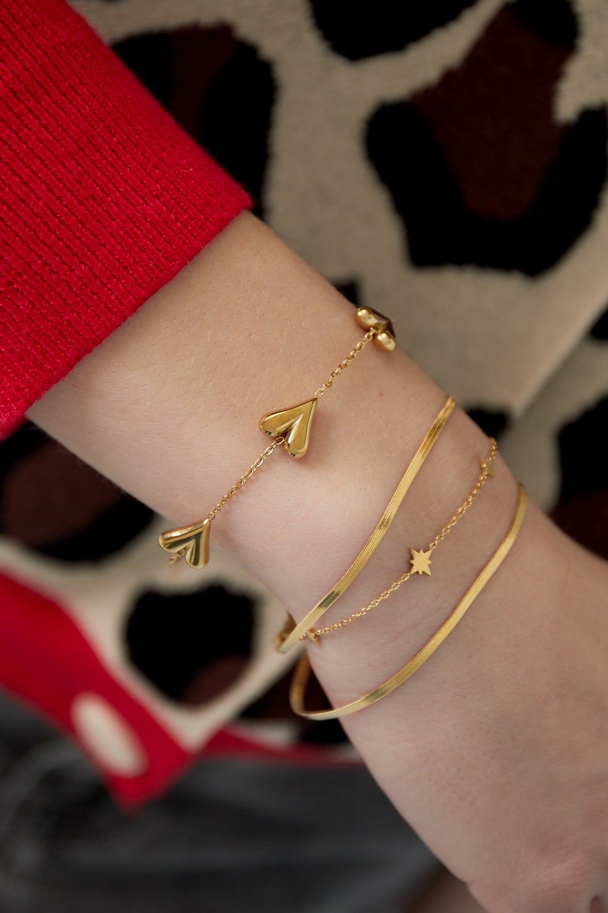 Stacked gold bracelets on wrist including the layered star charm bracelet and a heart-themed bracelet