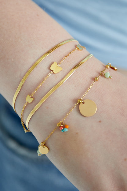 Close-up of a wrist wearing three gold bracelets including the butterfly charm bracelet layered with other delicate designs