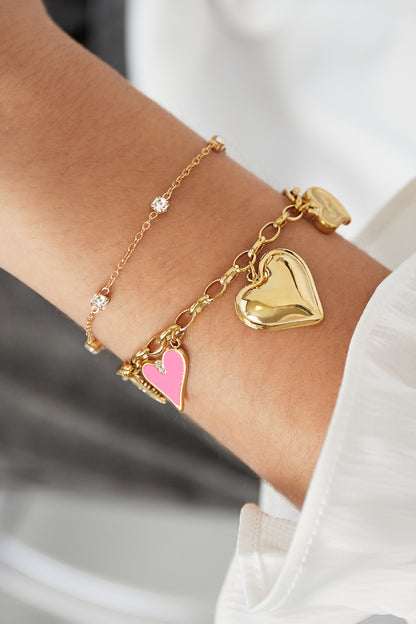 Close-up of a wrist wearing the gold crystal chain bracelet paired with a chunky gold heart charm bracelet