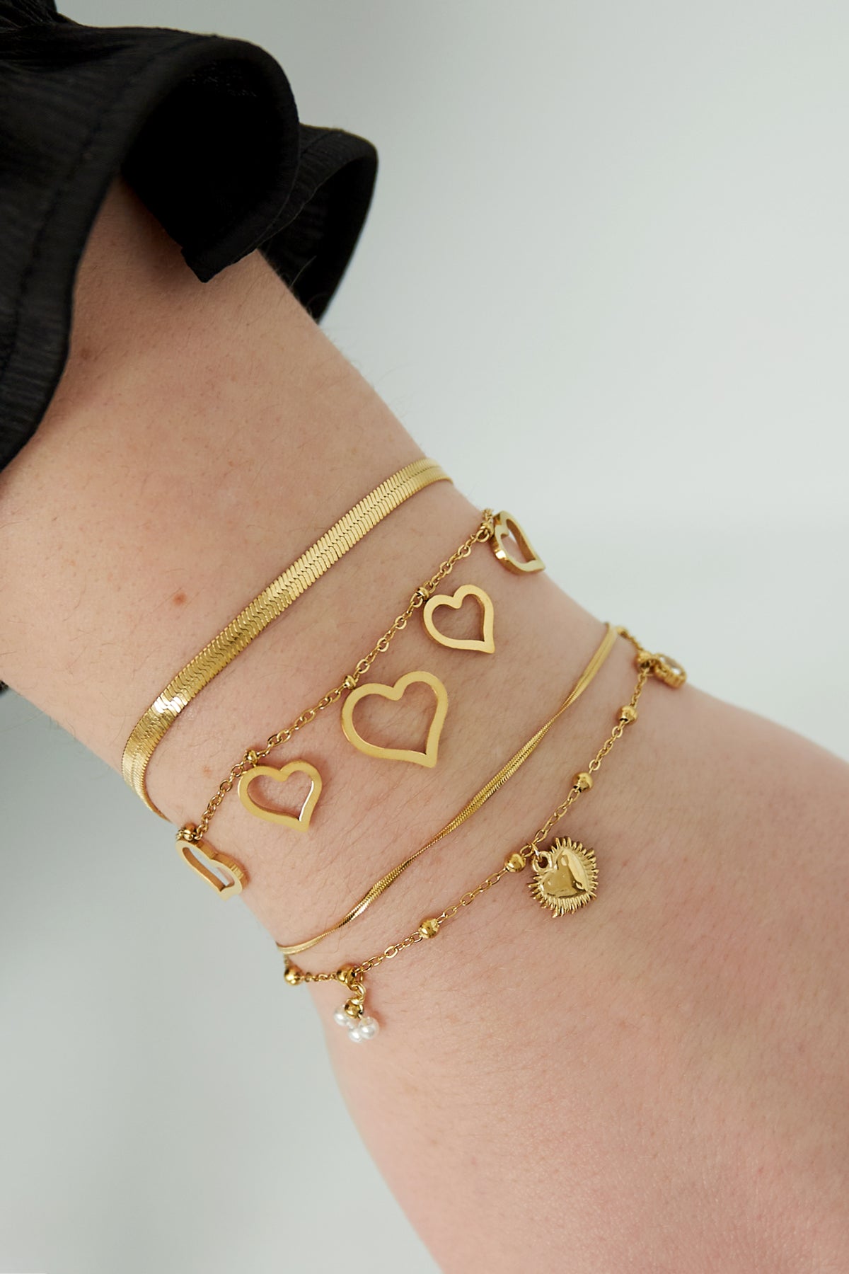 Close-up of wrist wearing stacked gold bracelets including a heart charm bracelet, showcasing elegant layering