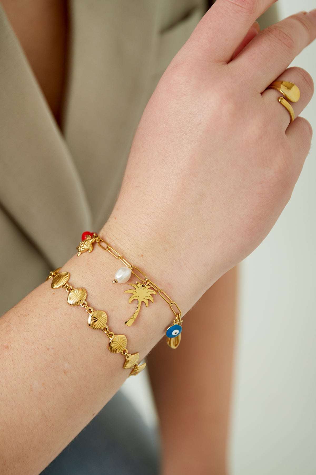 Close-up of the charm bracelet worn on a wrist, styled with a matching gold shell chain bracelet and a gold ring.