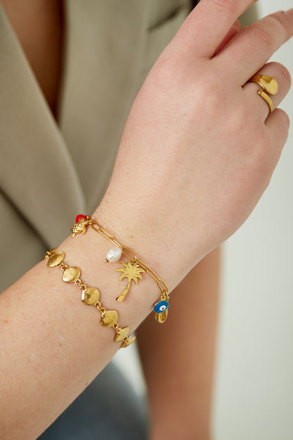 Close-up of the charm bracelet worn on a wrist, styled with a matching gold shell chain bracelet and a gold ring.