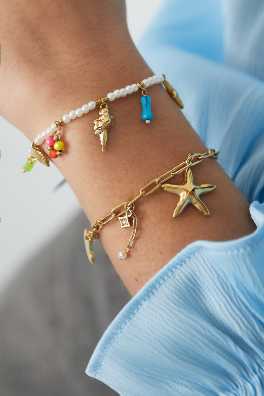 Close-up of wrist wearing a delicate pearl charm bracelet alongside a gold chain bracelet with starfish charm