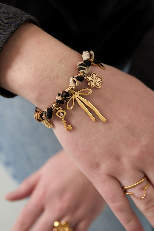 Woman’s wrist wearing leopard print bracelet adorned with gold-tone charms including a bow, key, and flower
