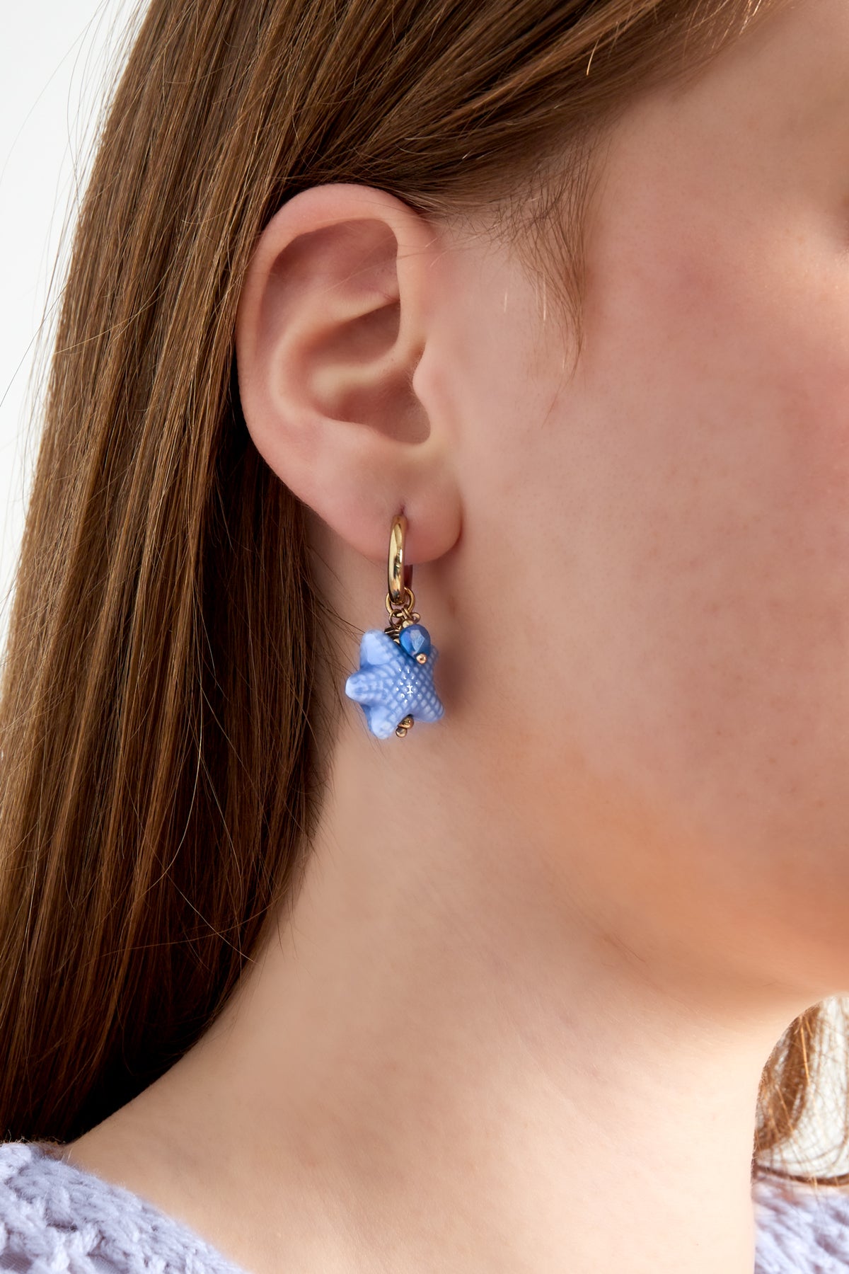 Woman wearing blue starfish charm hoop earring with gold hoop, showing minimal youthful style