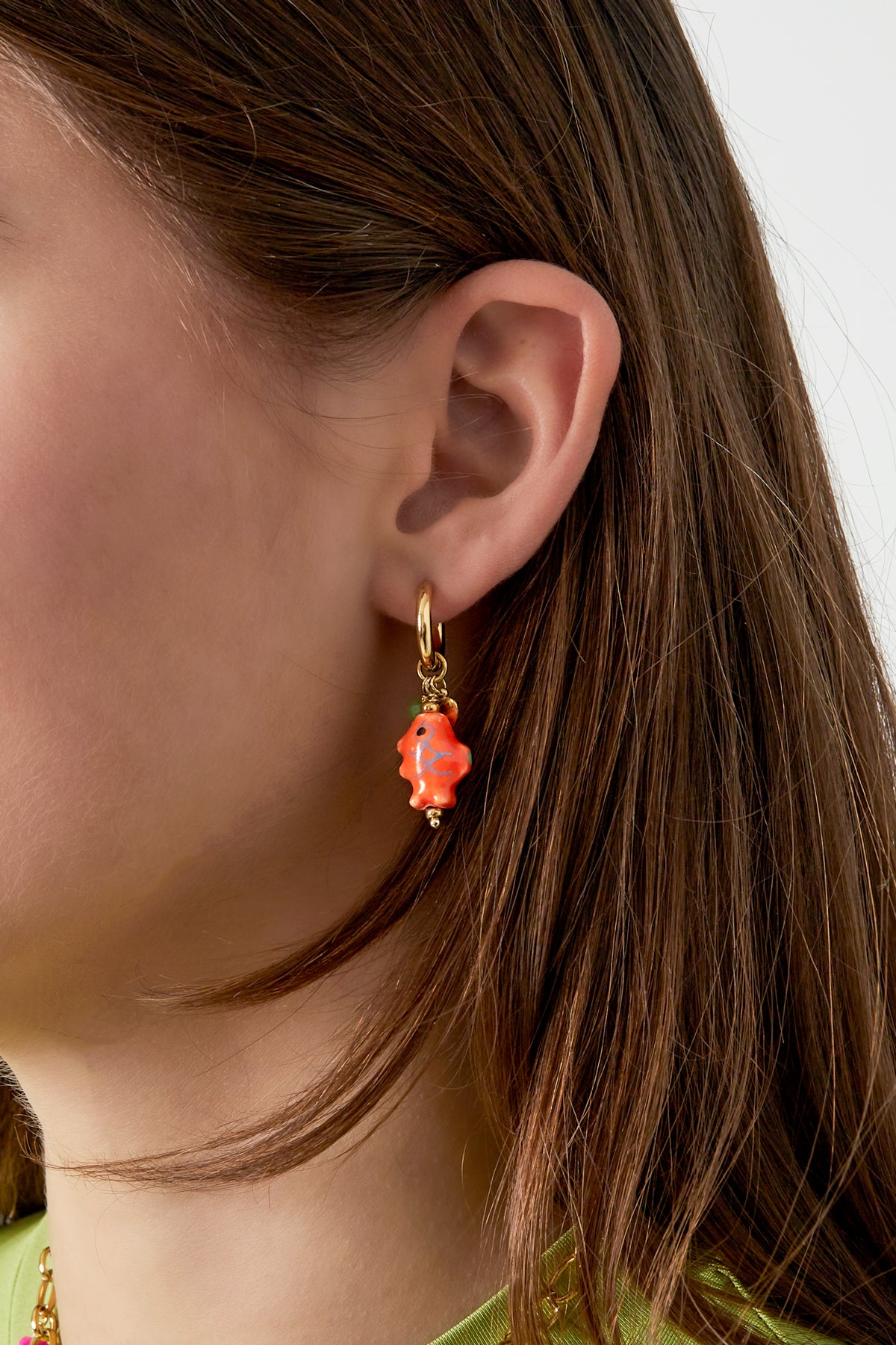 Close-up of a woman wearing gold-tone hoop earring with bright orange ceramic fish charm and small bead accents