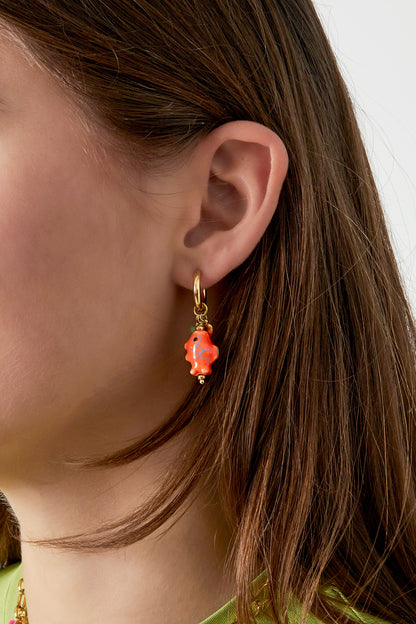 Close-up of a woman wearing gold-tone hoop earring with bright orange ceramic fish charm and small bead accents