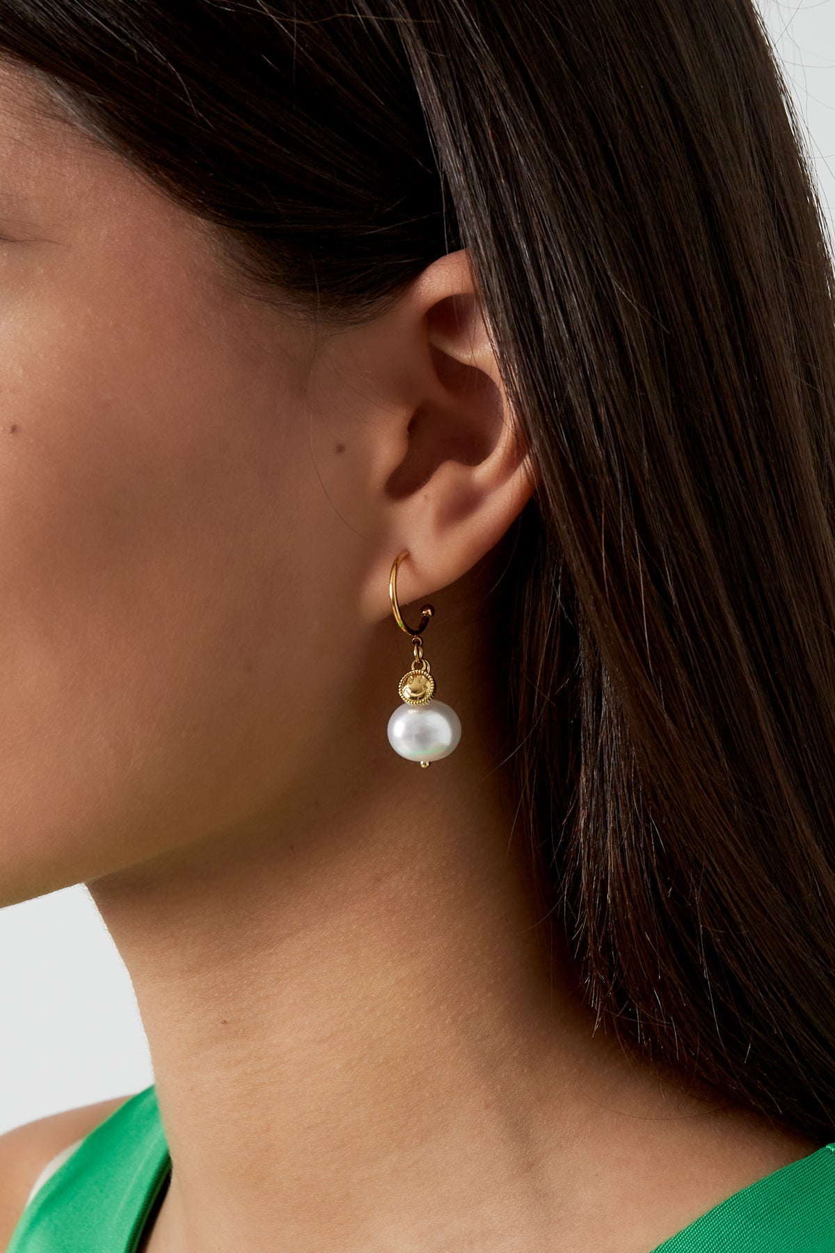 Close-up view of gold-tone Happy Glow drop earring worn by a model with dark hair and green top