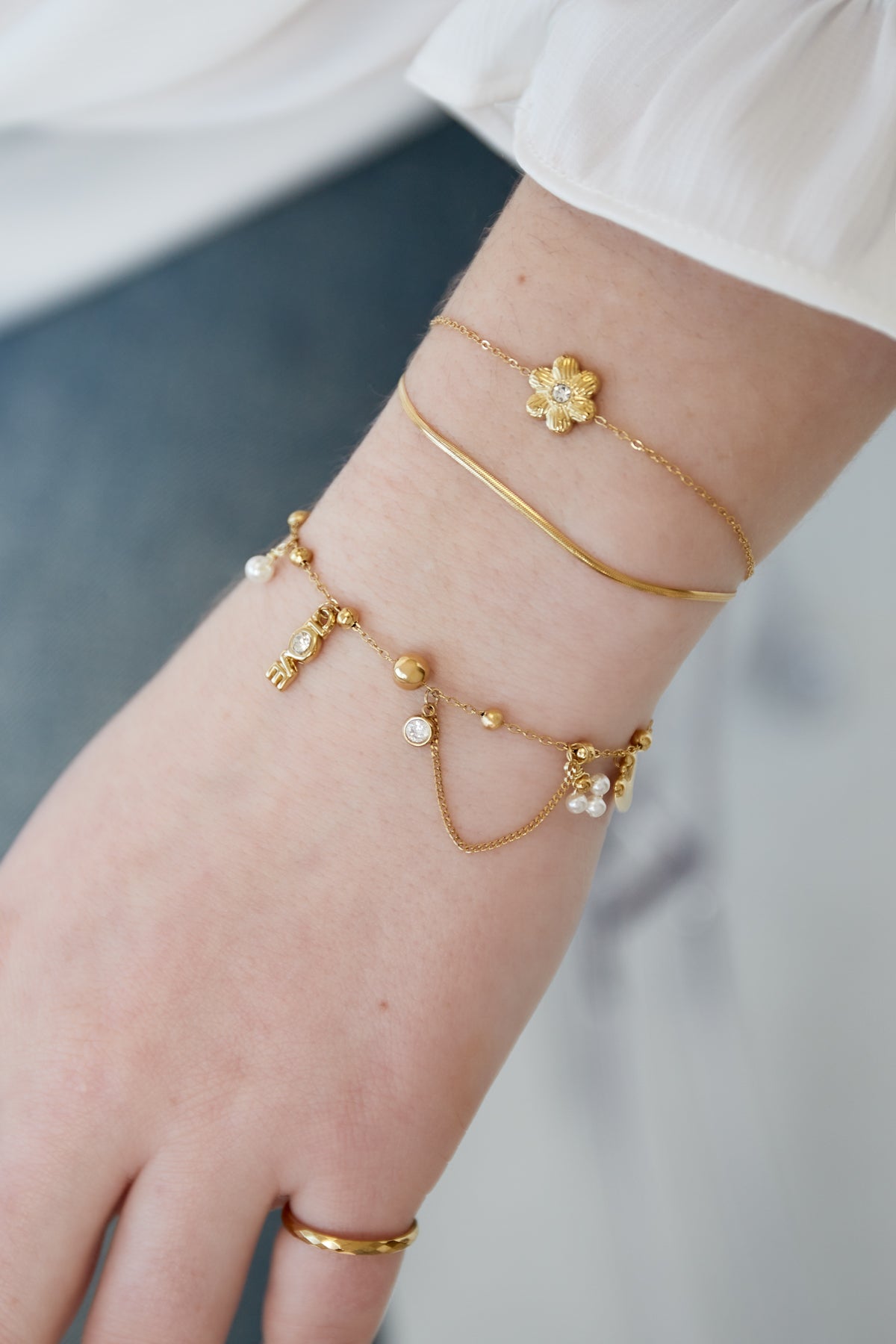 Model wrist wearing three bracelets including the gold charm bracelet showcasing the heart and LOVE charms with pearl accents