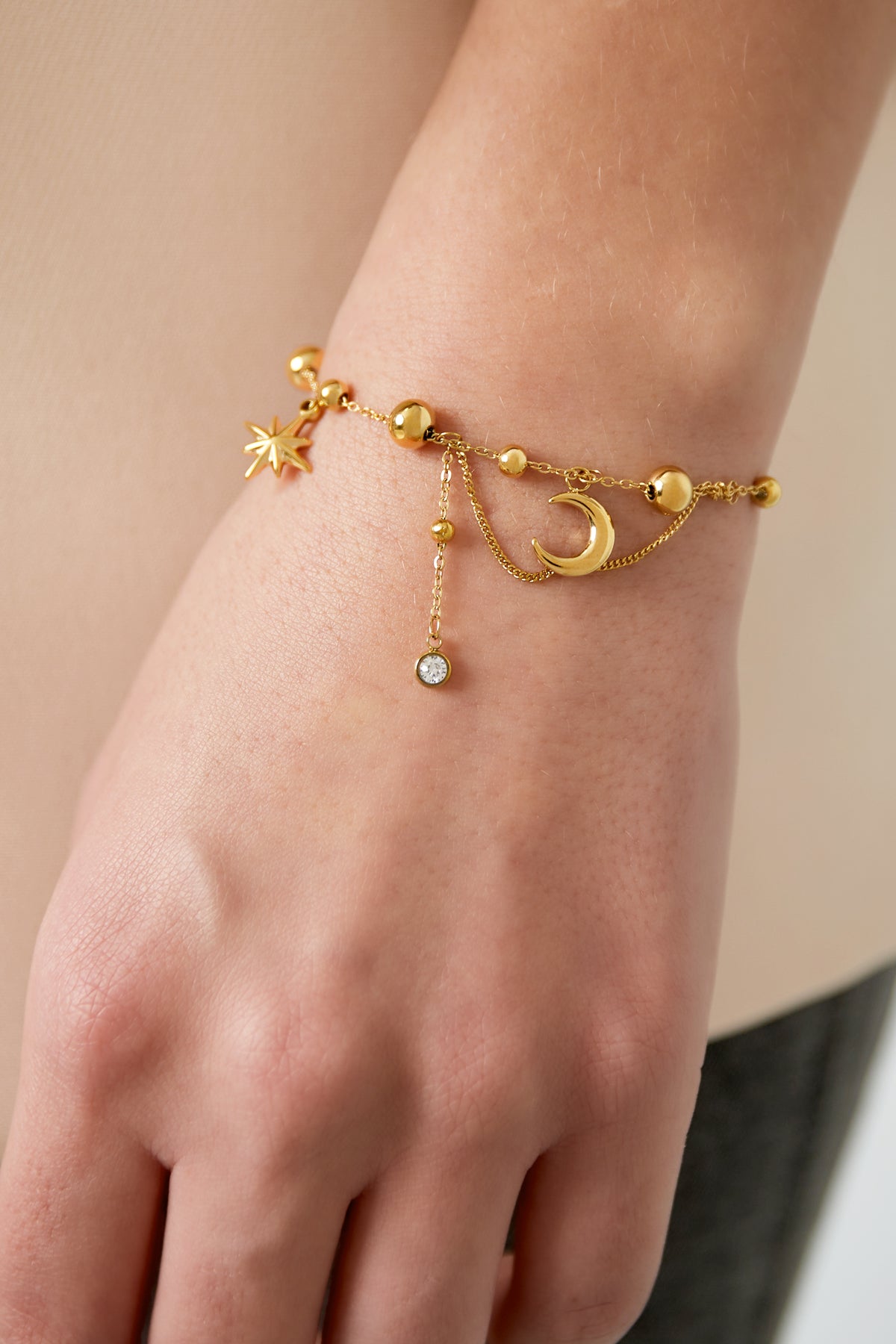 Gold celestial charm bracelet worn on wrist, showing delicate moon and star details with rhinestone dangles