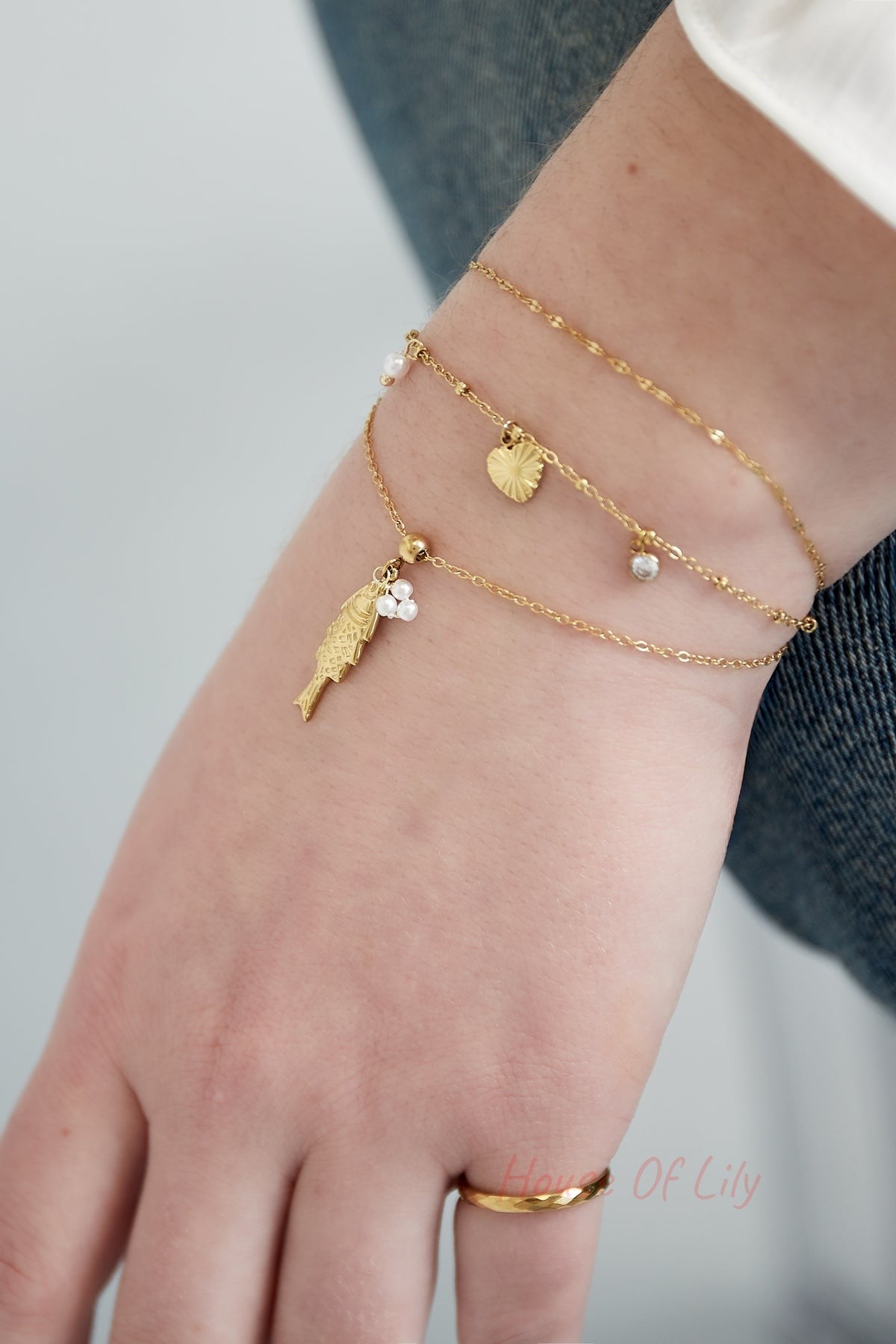 Woman's wrist adorned with layered gold tone delicate charm bracelets including a fish pendant and tiny shells and pearls