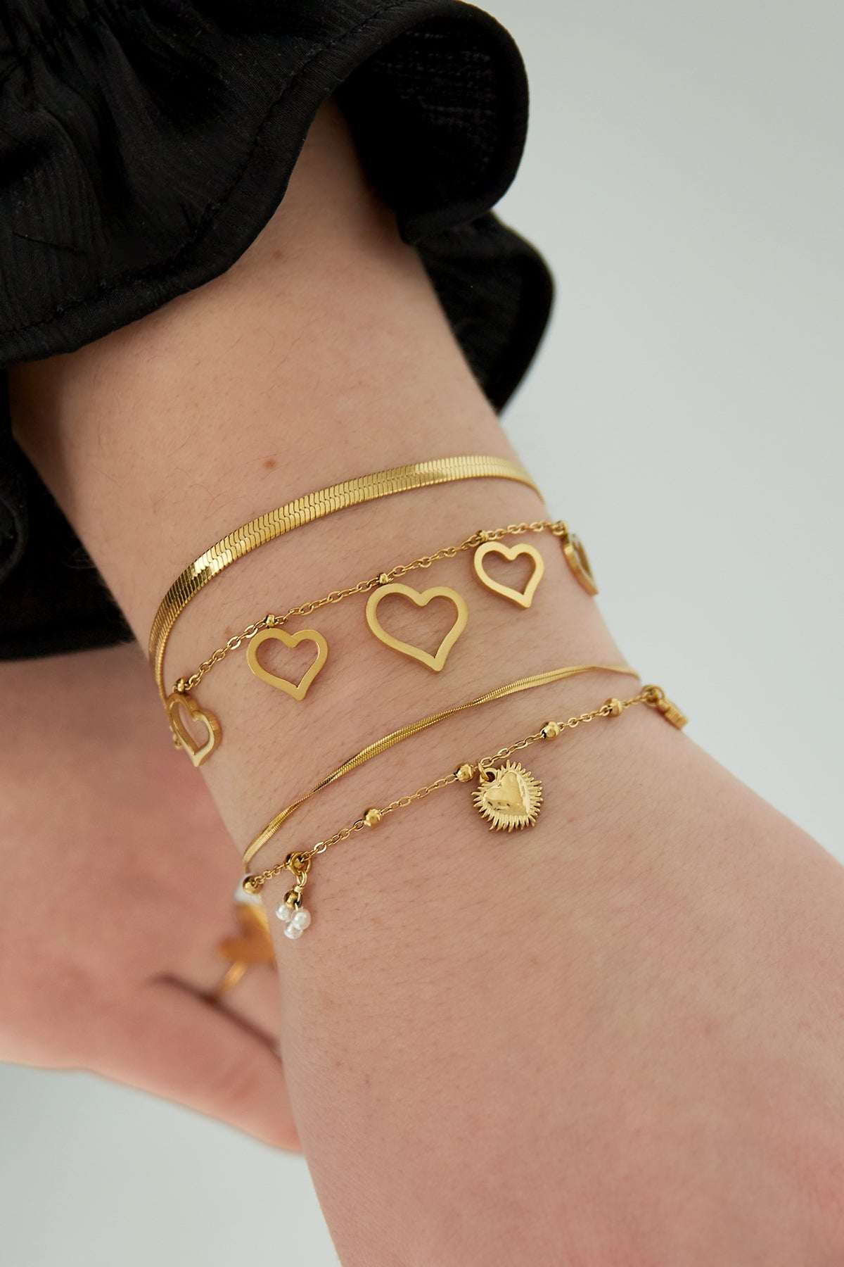Gold double heart charm bracelet styled on wrist with layered bracelets and black clothing