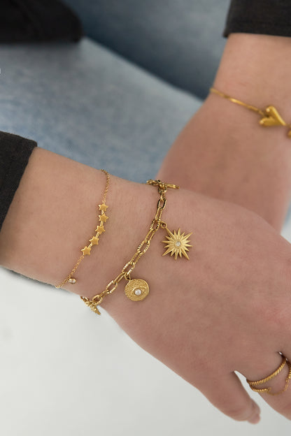 Wrist wearing layered bracelets featuring the gold star charm bracelet alongside two other gold charm bracelets on a woman's arm