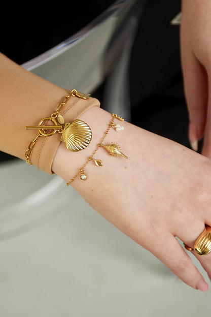 Model wearing layered gold charm bracelets featuring shell and pearl charms with ring