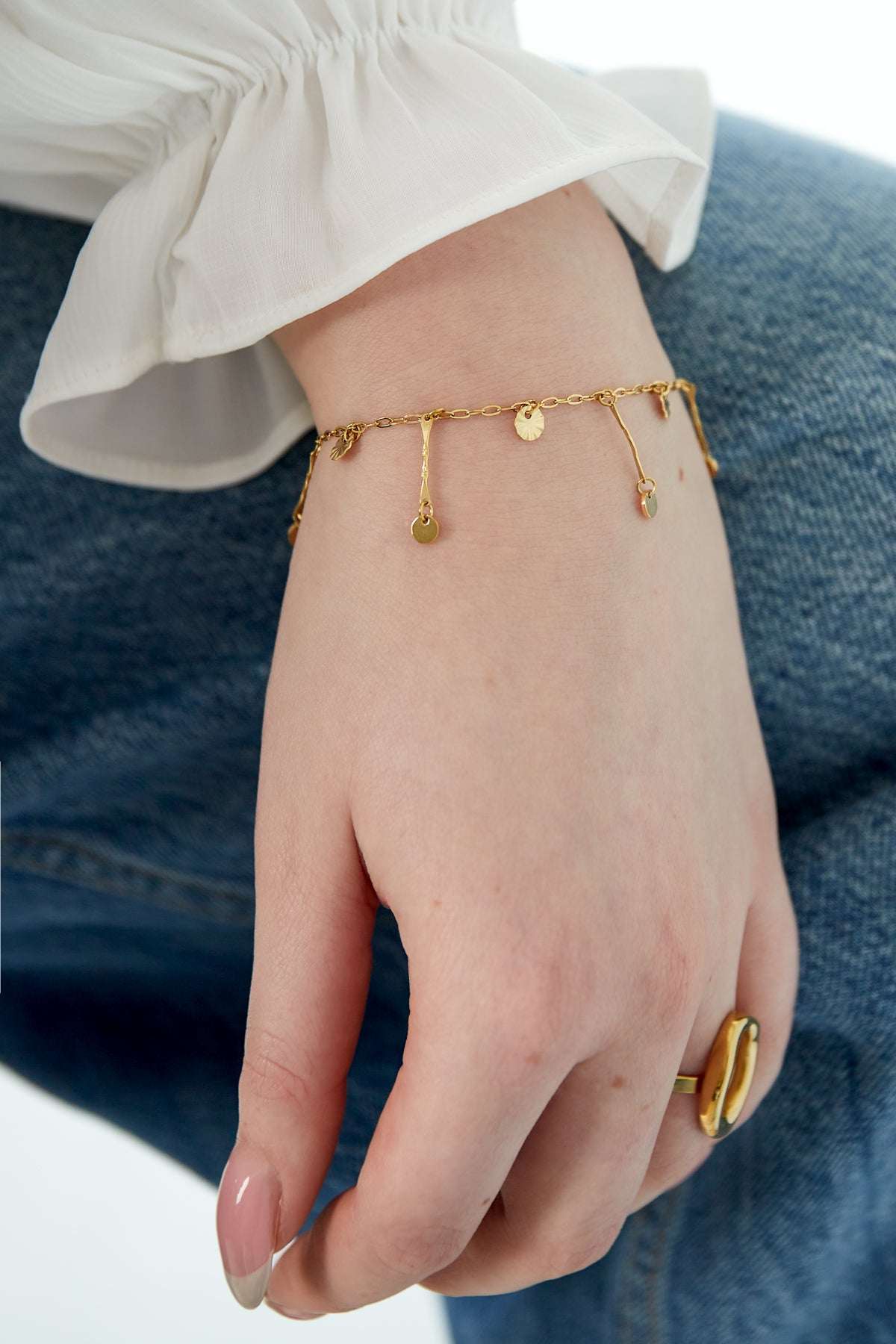Bracelet worn on wrist with white blouse sleeve and denim, highlighting dainty gold coin charms