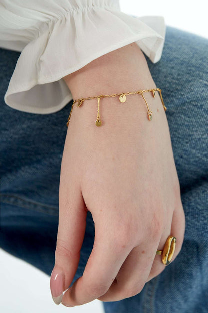 Bracelet worn on wrist with white blouse sleeve and denim, highlighting dainty gold coin charms