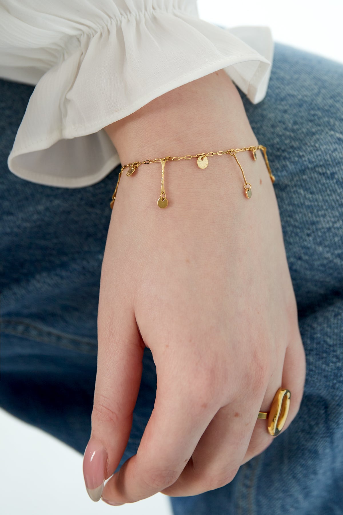 Bracelet worn on wrist with white blouse sleeve and denim, highlighting dainty gold coin charms