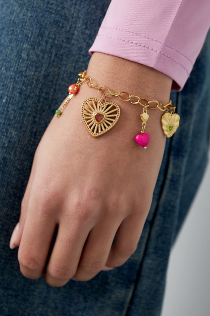 Close-up of gold charm bracelet worn on wrist with pink cuff and denim showcasing vibrant charms