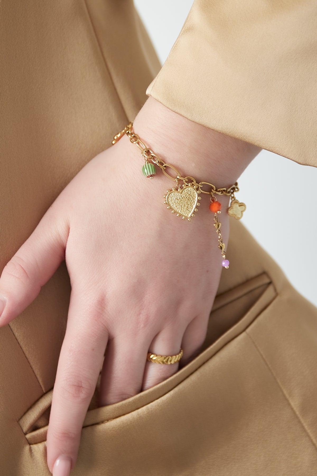 Close-up of bracelet worn on wrist alongside a gold ring and camel coloured sleeve