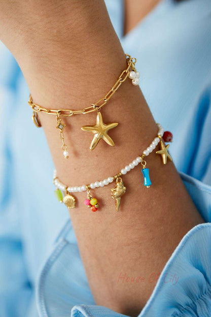 Close-up of two stacked charm bracelets on wrist including gold-tone seaside charm bracelet with starfish and pearl details and colourful beaded bracelet