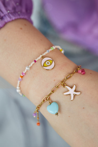 Model wearing gold charm bracelet with starfish and heart charms paired with a colorful beaded bracelet on wrist