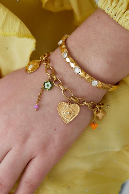Close-up of gold charm bracelet worn on wrist with yellow blouse, showing detailed charms and glossy finish