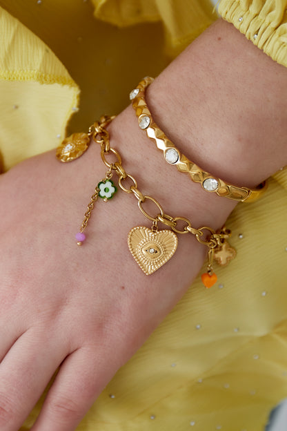 Close-up of gold charm bracelet worn on wrist with yellow blouse, showing detailed charms and glossy finish
