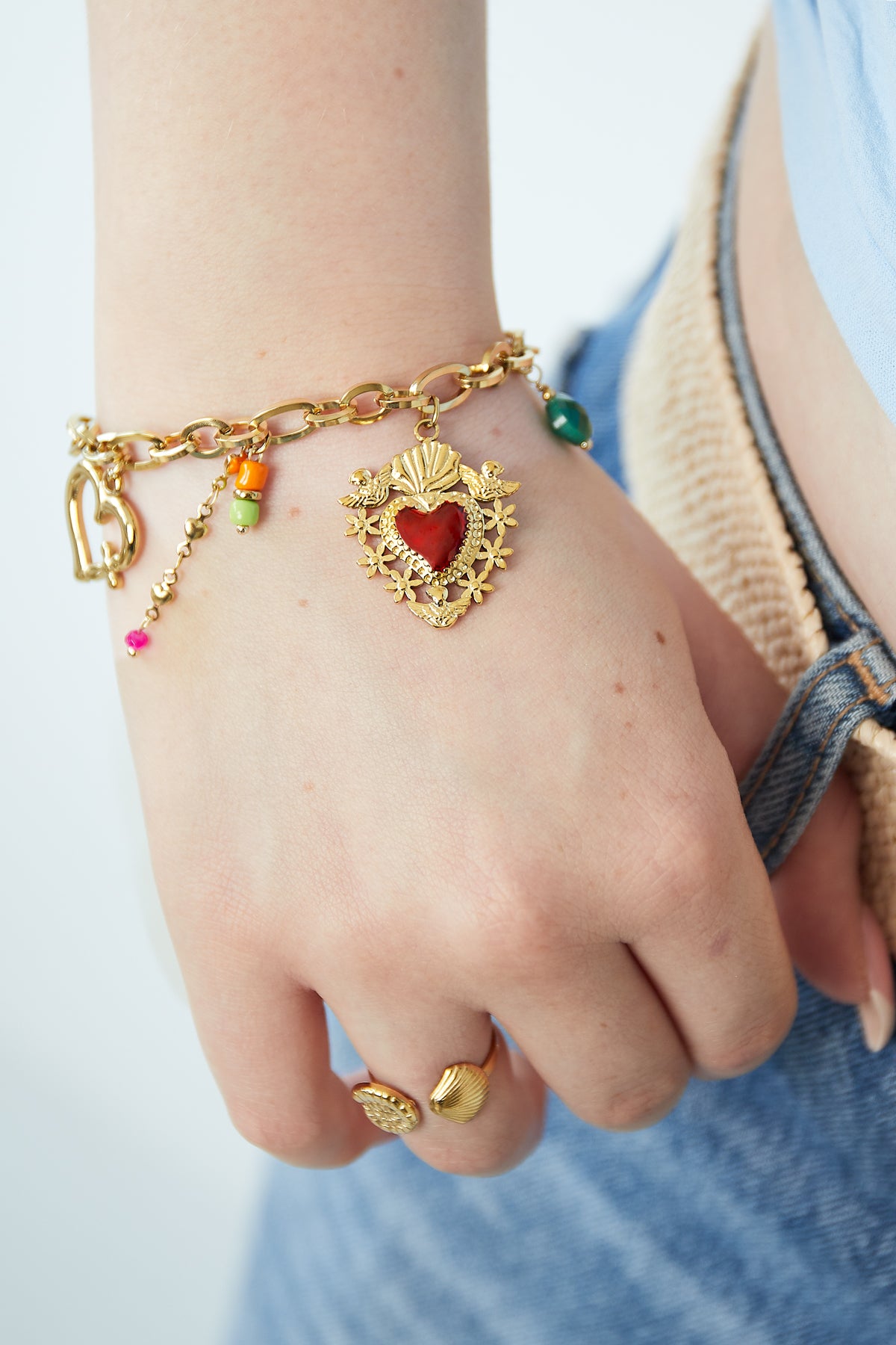 Close-up of the gold charm bracelet worn on wrist with matching gold shell ring and casual outfit details