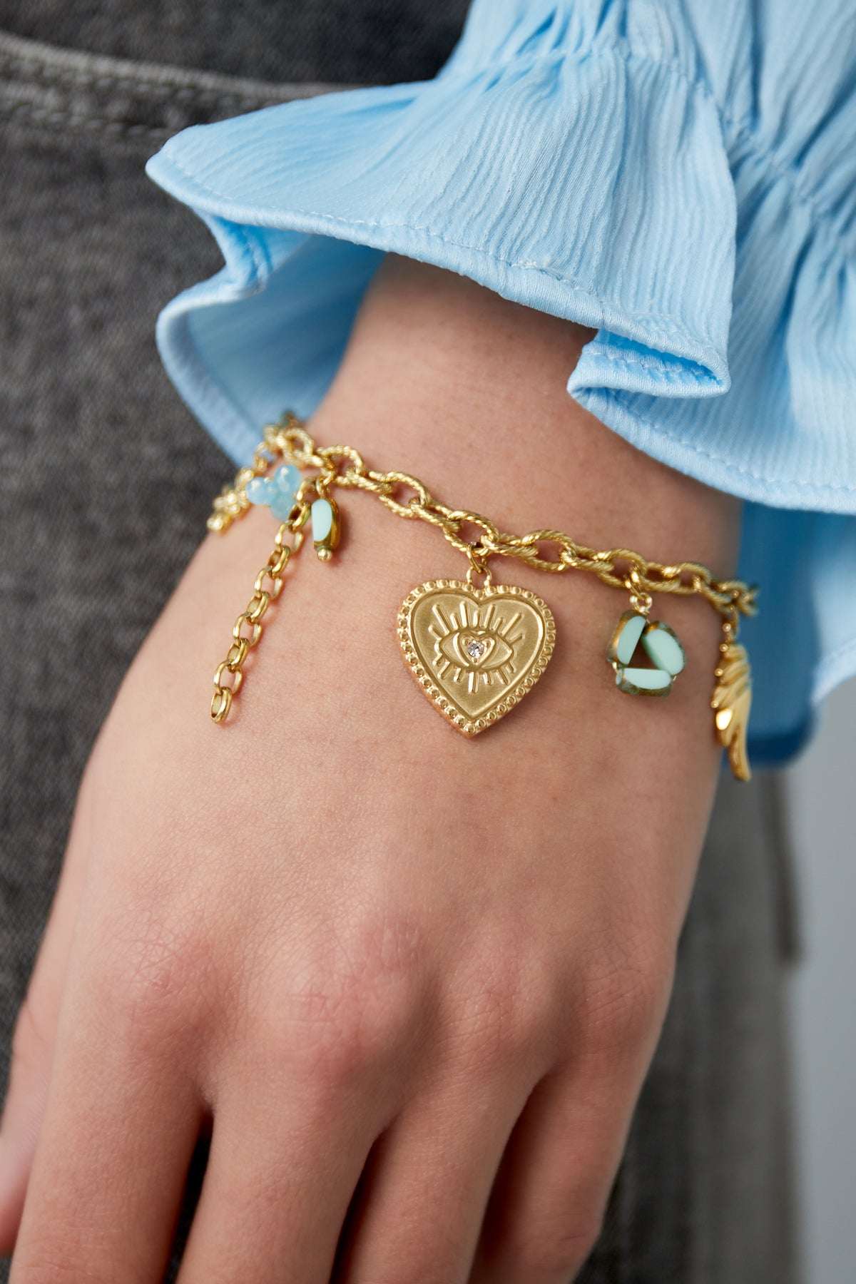 Golden charm bracelet worn on wrist paired with blue fabric sleeve highlighting the playful charms and textured chain links