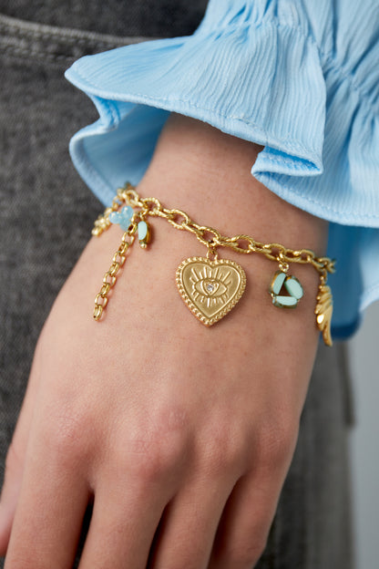 Golden charm bracelet worn on wrist paired with blue fabric sleeve highlighting the playful charms and textured chain links