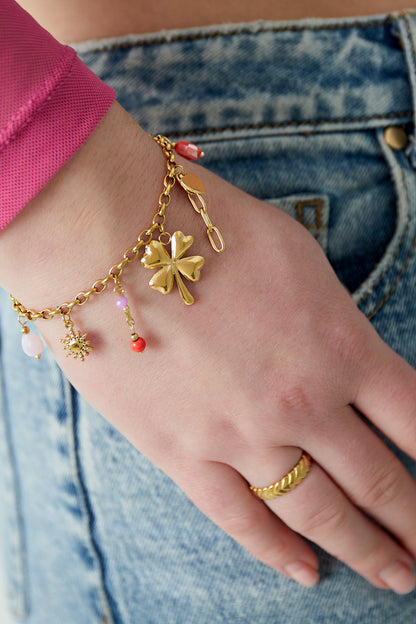 Close-up of gold charm bracelet with four-leaf clover, sun, heart and colourful beads worn on wrist with denim jeans
