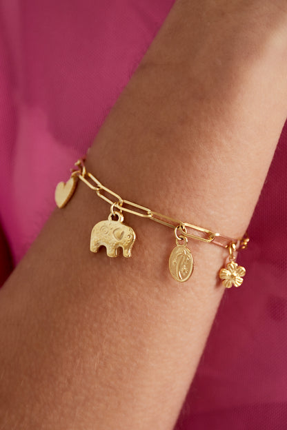 Close-up of golden charm link bracelet worn on wrist showing detailed elephant and flower charms against a pink background