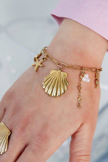 Close-up of golden shell charm bracelet worn on wrist with pink sleeve background