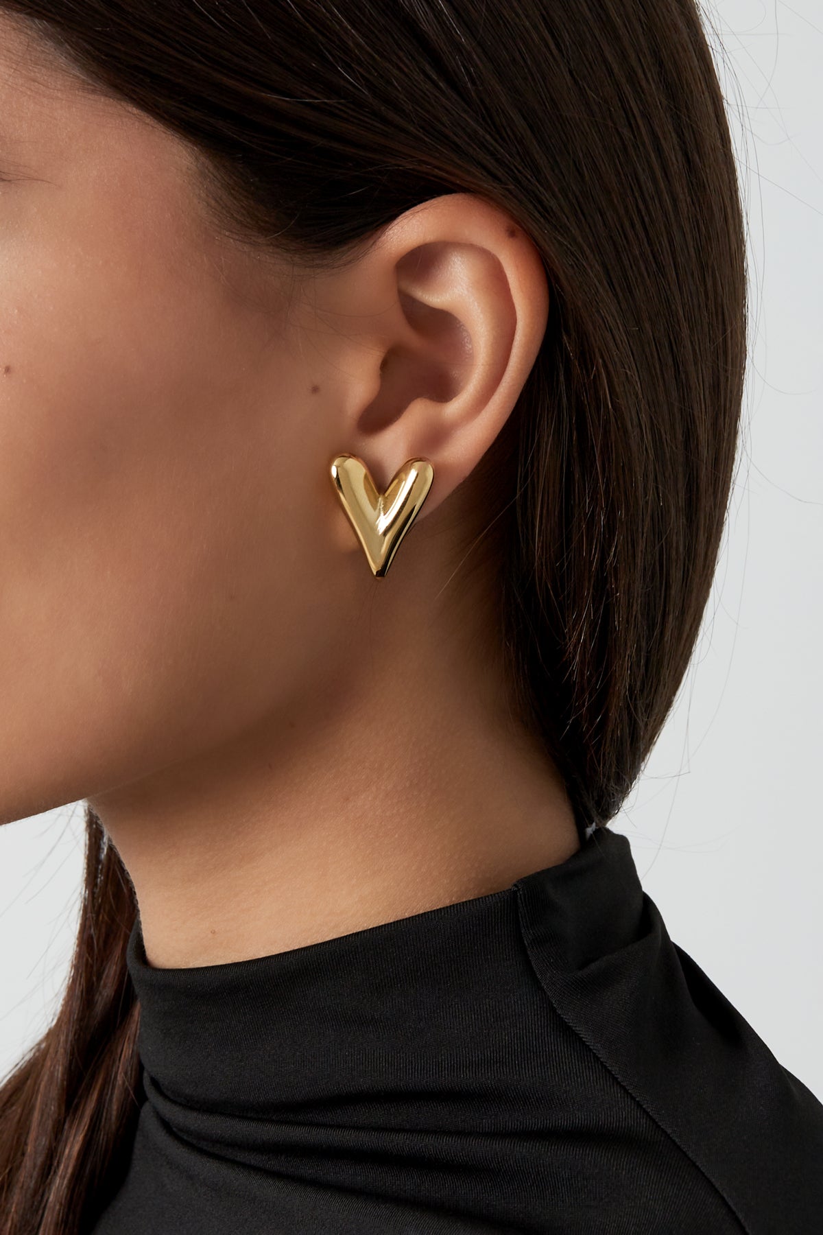 Close-up of a woman wearing gold heart stud earrings paired with a black top