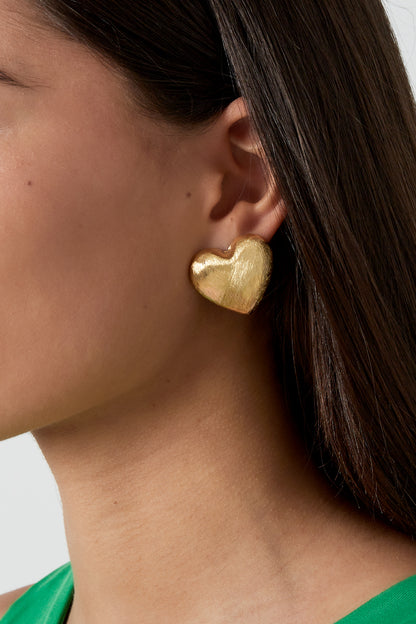 Close-up of a woman wearing brushed gold heart stud earring with smooth dark hair and green top