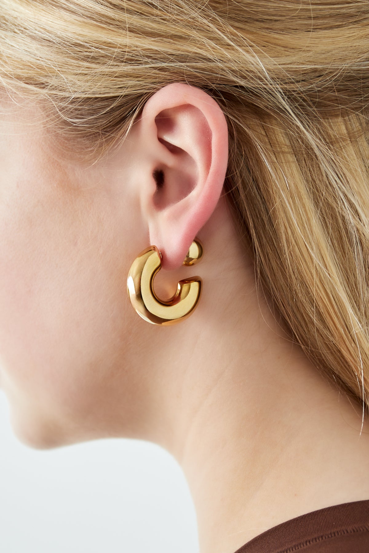 Close-up of woman wearing chunky gold hoop earring showing bold silhouette and polished finish