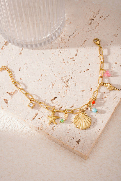 Golden sea charm bracelet laid flat on textured stone surface with sunlight highlighting colourful bead details