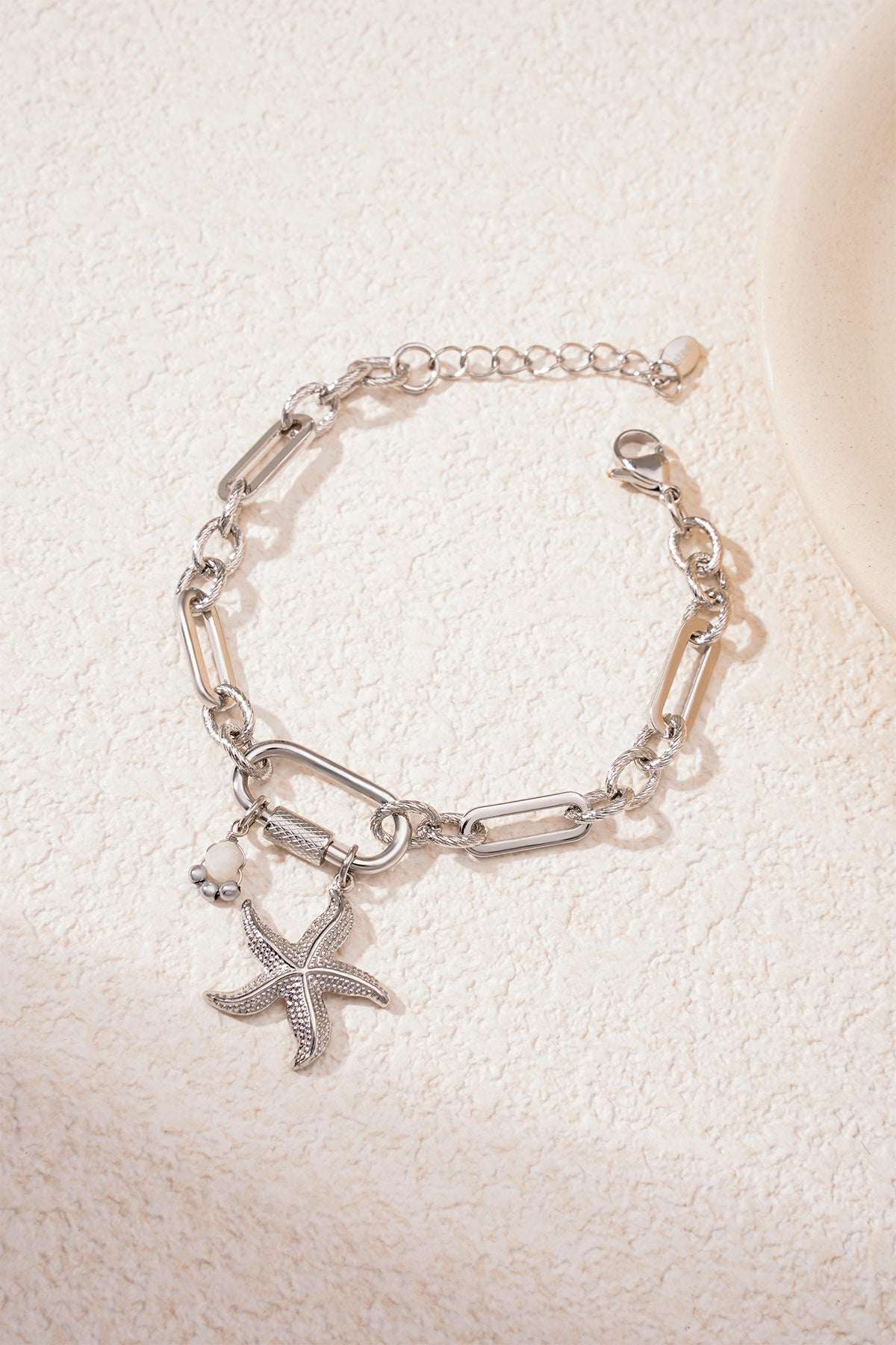 Silver starfish charm bracelet on textured light surface