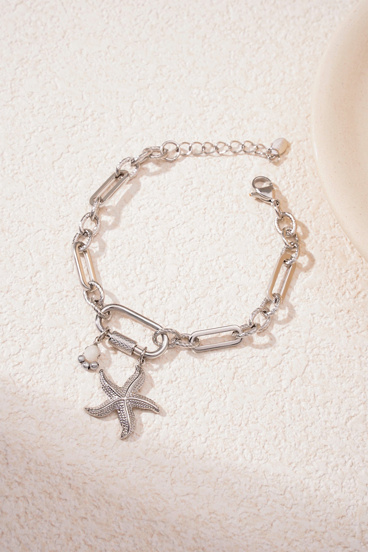 Silver starfish charm bracelet on textured light surface