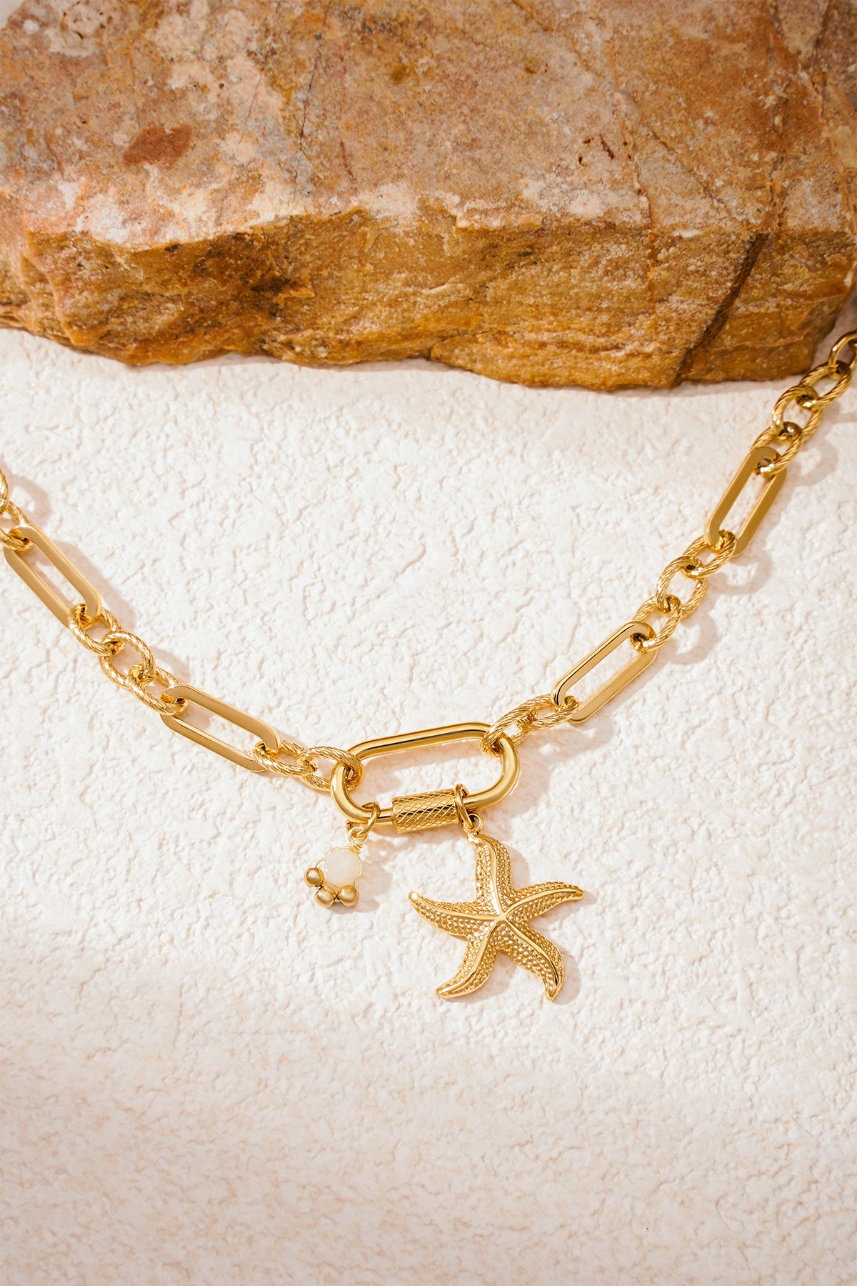 Close-up of gold and silver starfish charm bracelets placed side by side on textured surface
