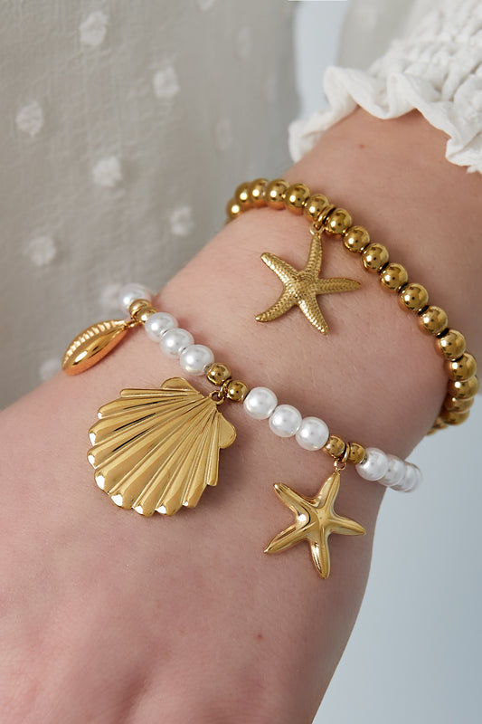 Two layered bracelets on a wrist: one with gold-tone beads and starfish charm, and the other with white pearls and three gold-tone sea charms