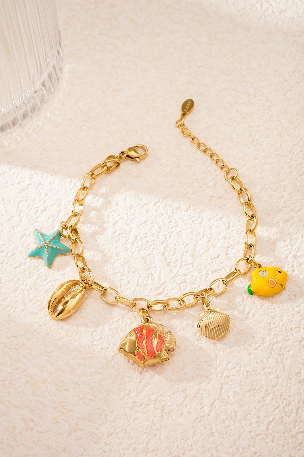 Playful ocean-themed charm bracelet lying flat on sandy textured surface with vibrant turquoise starfish charm