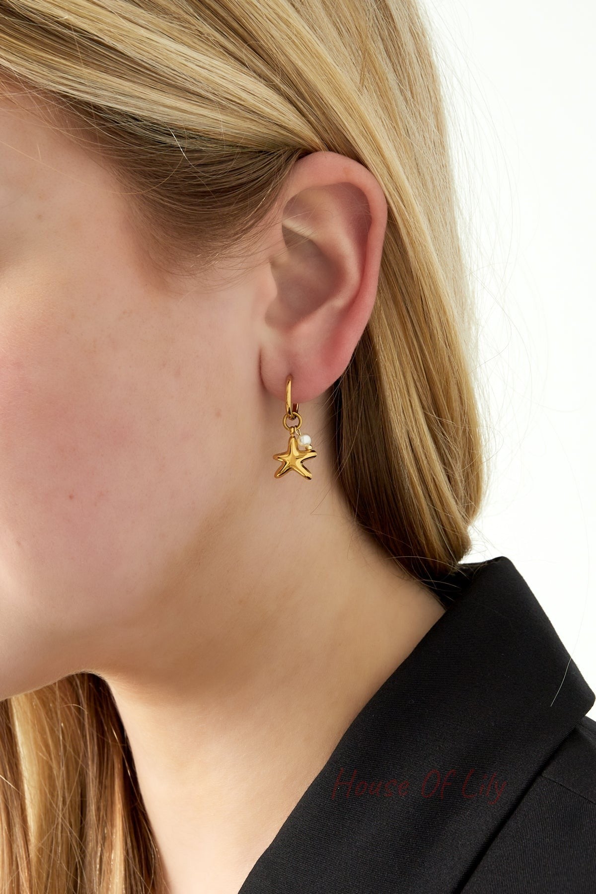 Close-up side view of gold starfish charm hoop earring worn by a woman with blonde hair and black top