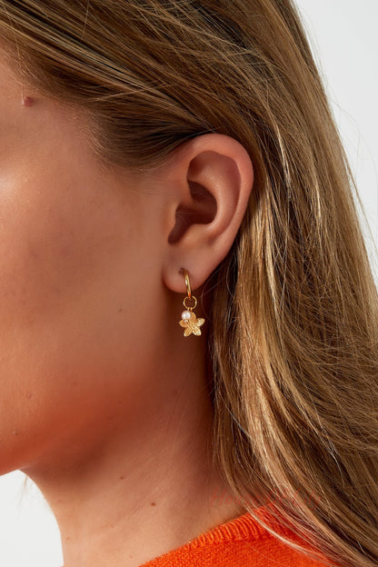 Close-up of gold floral charm hoop earring worn on a woman's ear with blonde hair and orange sweater