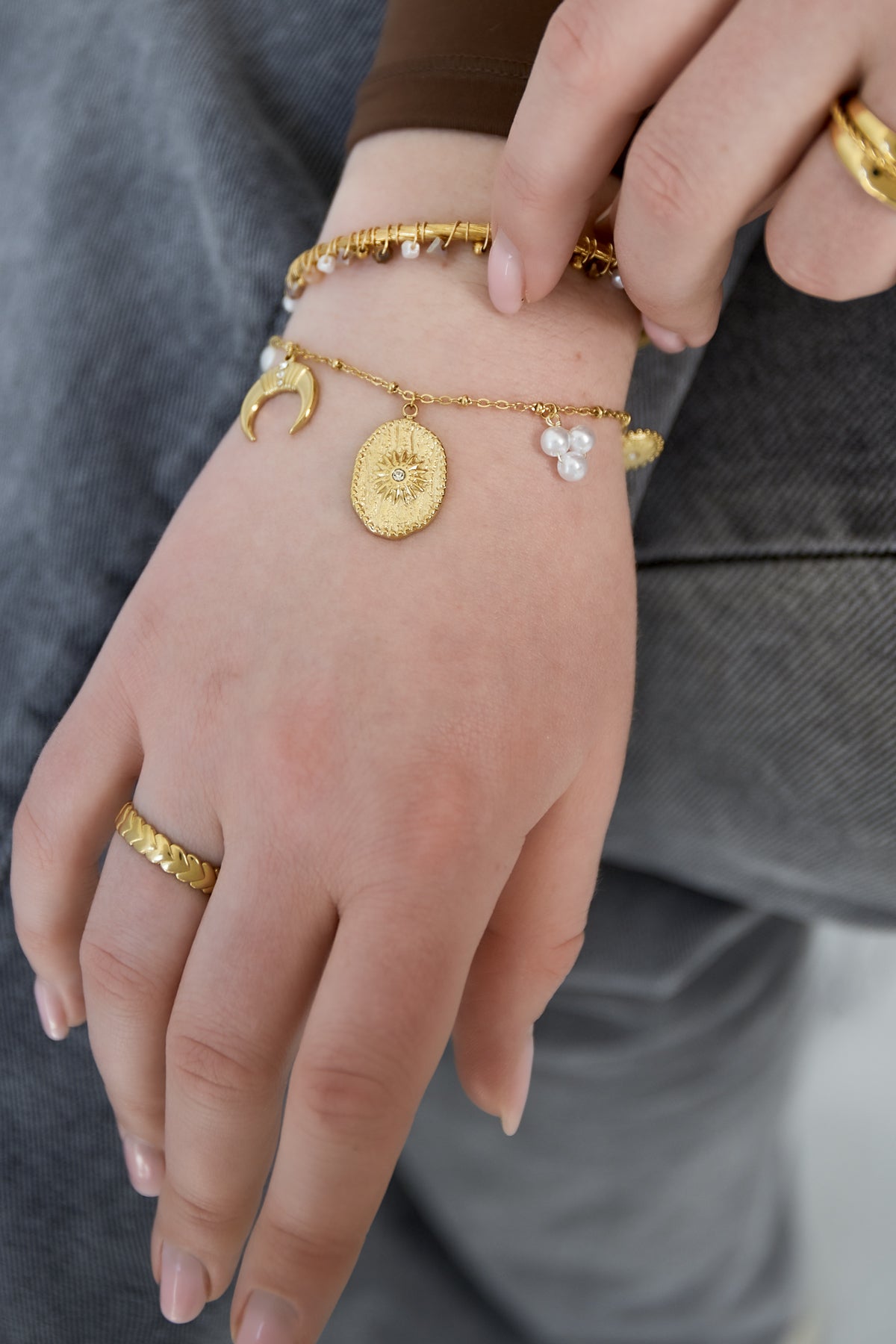 Close-up of hand wearing gold crescent moon charm bracelet with textured medallion and pearl cluster