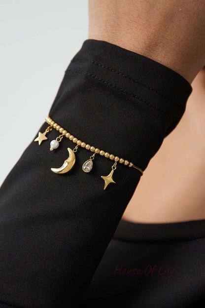 Gold celestial charm bracelet worn on wrist with black fabric background highlighting charms and beaded design