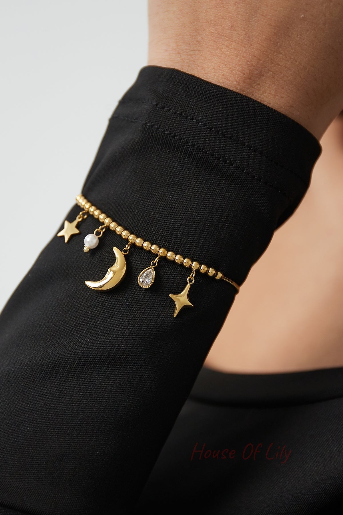 Gold celestial charm bracelet worn on wrist with black fabric background highlighting charms and beaded design